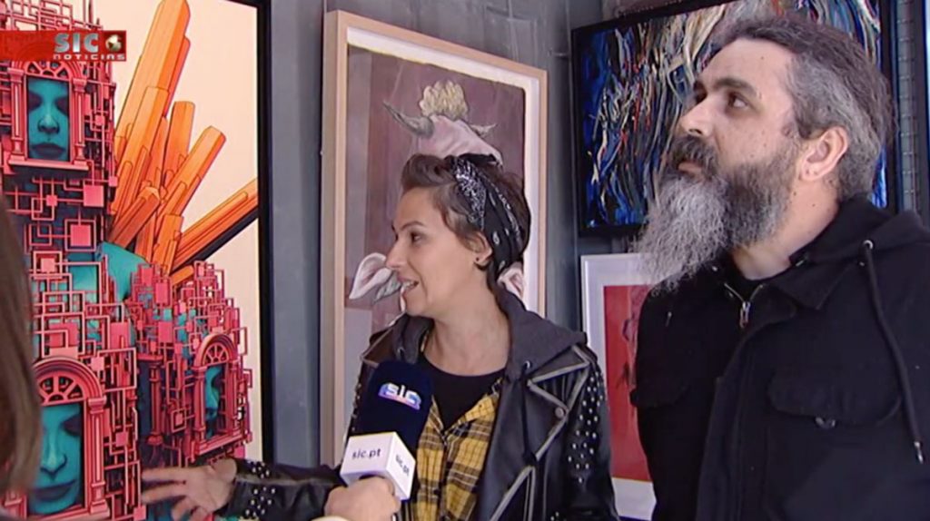 Tânia and Lucas in front of paintings talking to a reporter